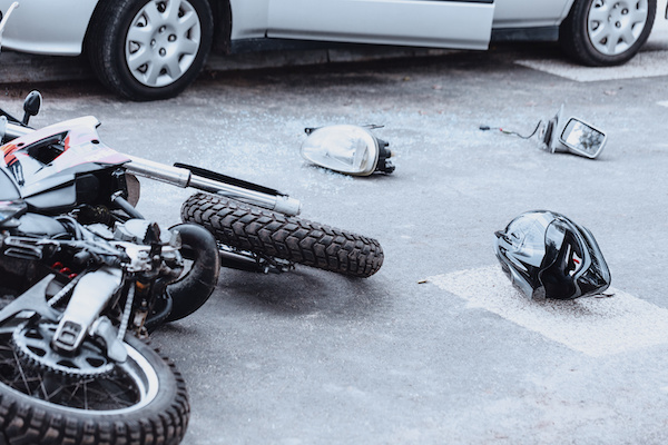 Bike, helmet and crash debris in the street near a car, indicating a a serious motorcycle accident.