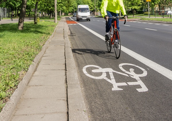 Cyclist in a bright jacket riding in a marked bike lane on a city street with a van approaching in the background.