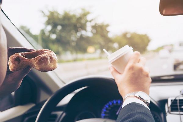 Man eating donuts with coffee while driving car.