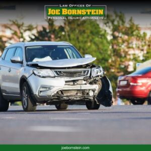 A grey vehicle with front end damage sits in the road after a car accident in Portland, ME