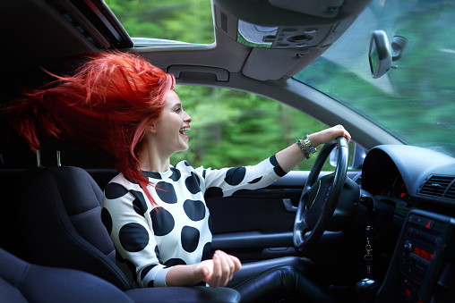 Teen girl driving fast with the sunroof down and her red hair blowing in the wind.