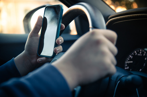 Teen reading text messages holding a cell phone while driving.