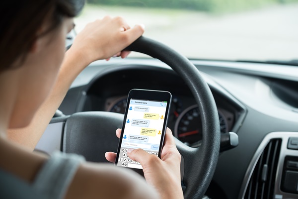 Close-up of a teen driver holding a cell phone and reading text messages while she's driving.